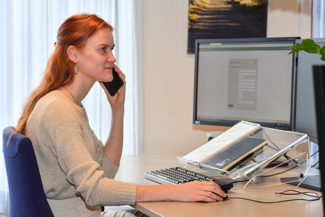 Vrouw zit achter computer met een telefoon aan het oor